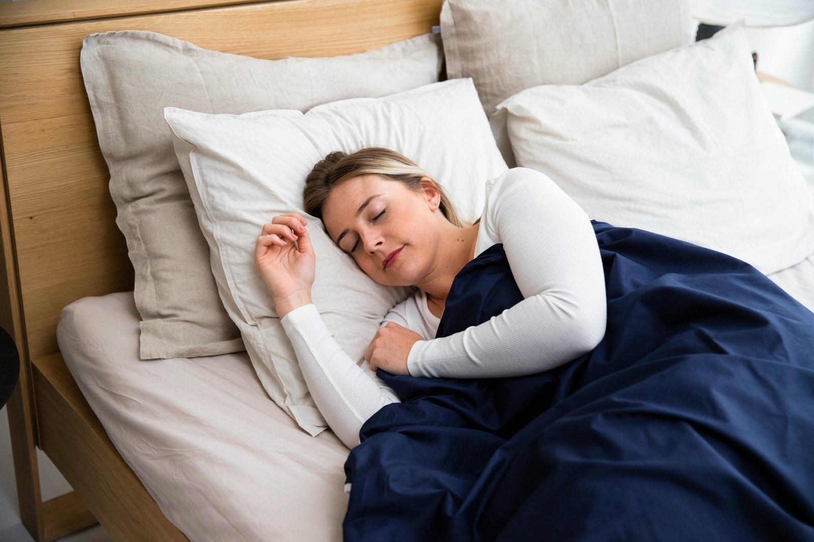 Woman peacefully sleeping in a cozy bedroom with white pillows and dark blue duvet.